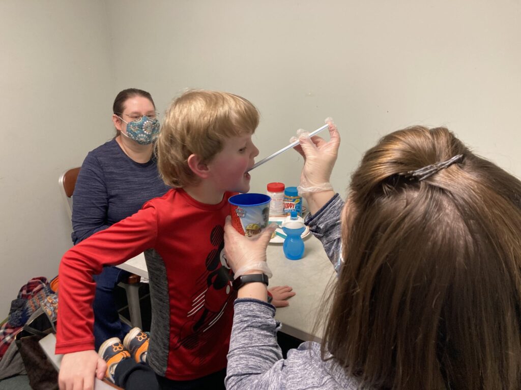 Carter drinking some nutrition drink from a straw held by a therapist.