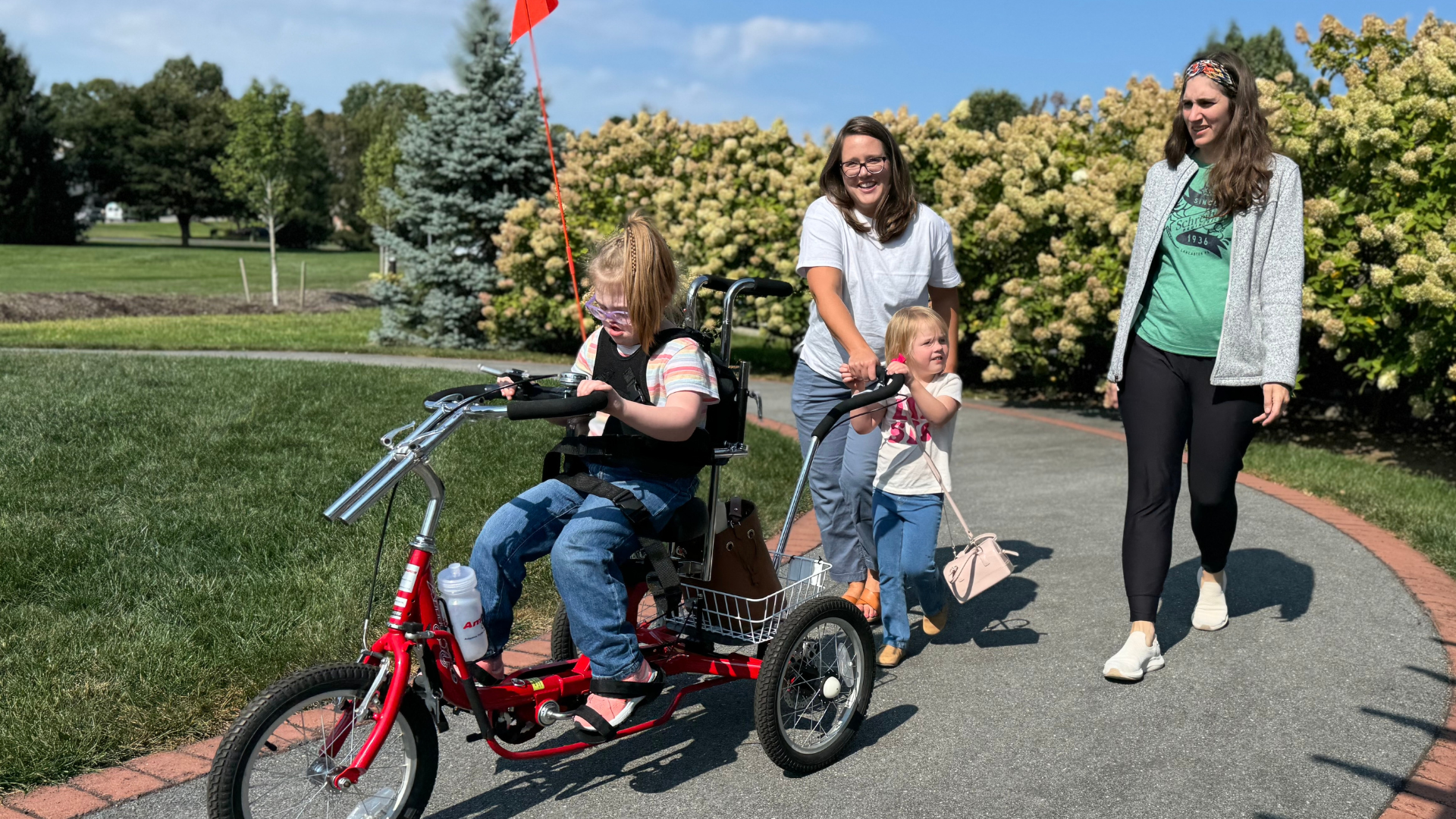 Women walking with child behind a child on an adaptive tricycle.