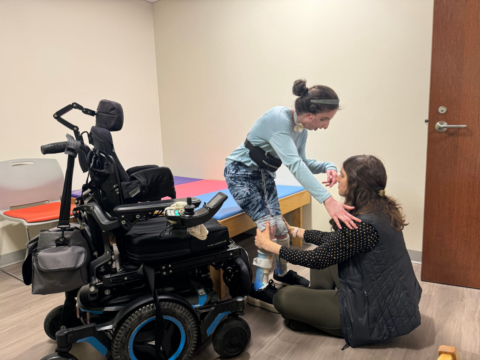 Woman helping child into wheelchair.