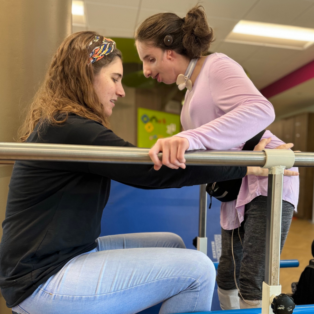 Child utilizing guide rails to stand and move forward with the assistance of a therapist.