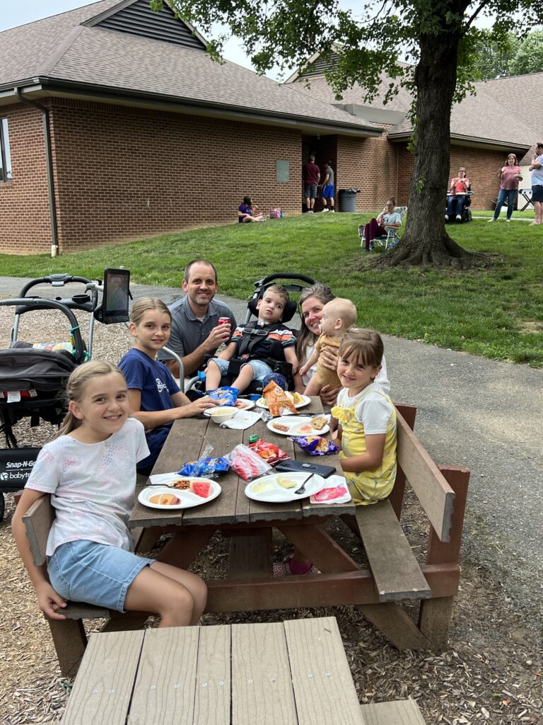 A family with five children around a picnic table, smiling and eating.