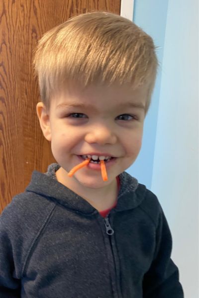 Finn smiling with two small carrots hanging out of his mouth. 