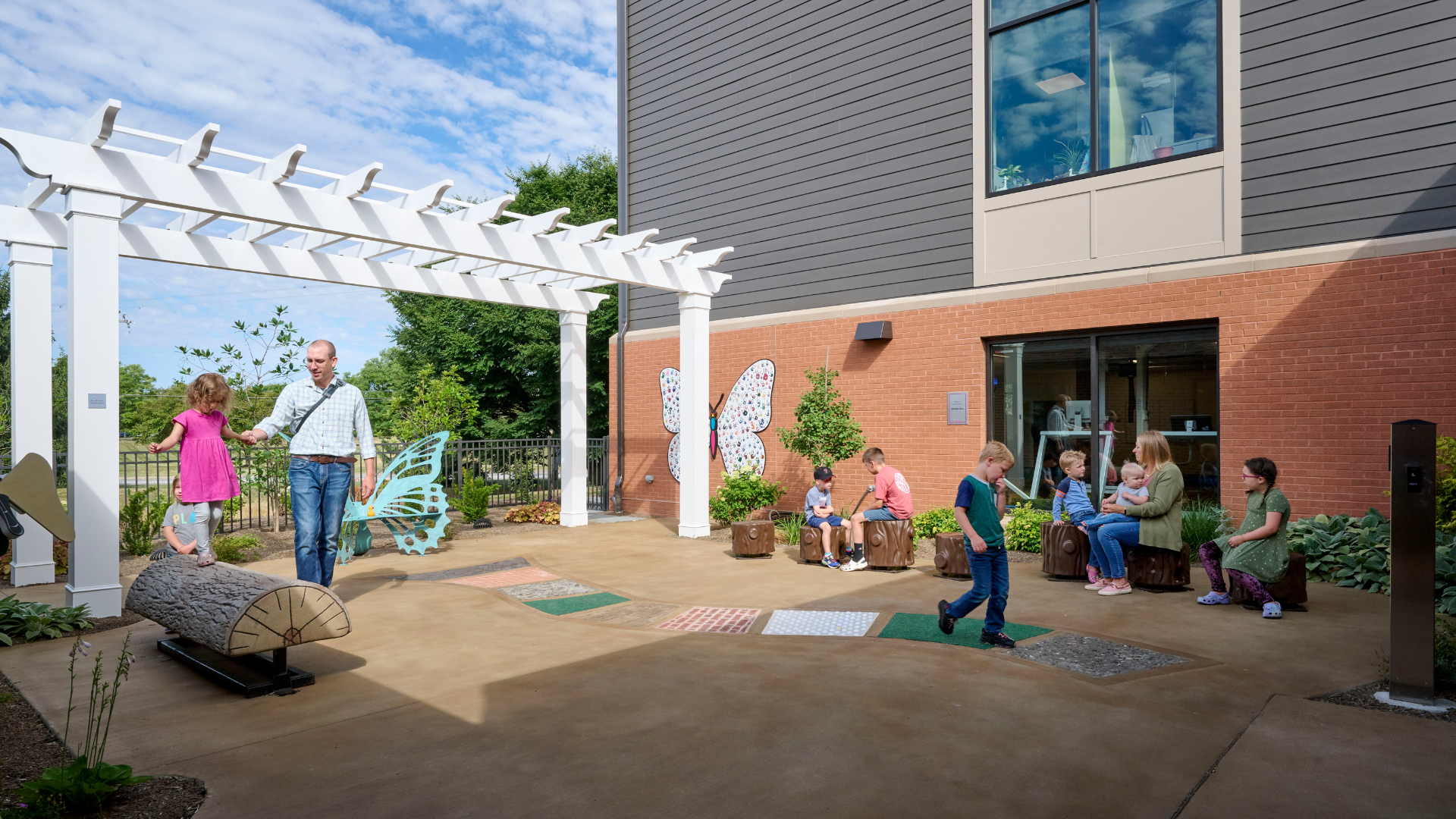 A sunny day at the outdoor play and exercise area at Schreiber Pediatric Center where adults and children utilize woods themed equipment.