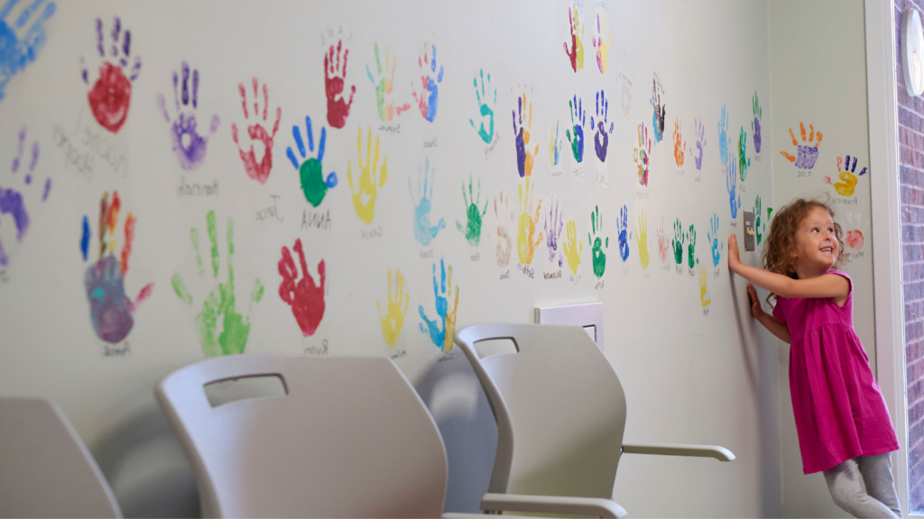 Young girl making handprints on wall with paint.