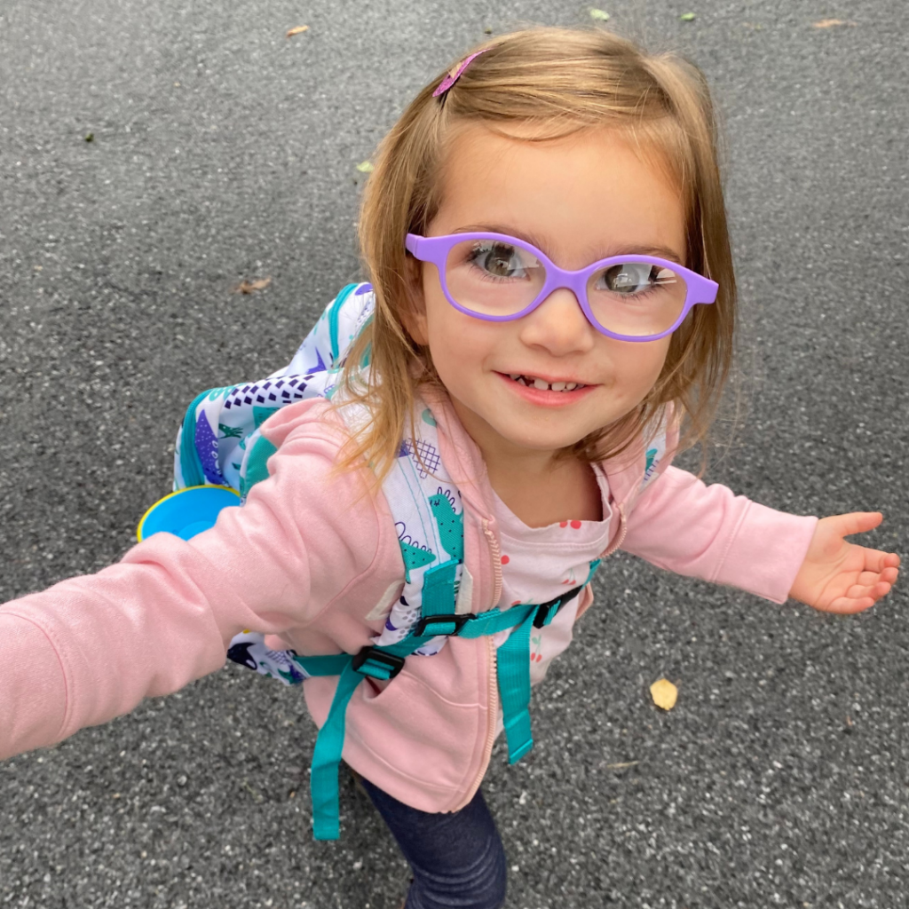 Harper looking up and smiling while walking on pavement wearing a blue backpack.