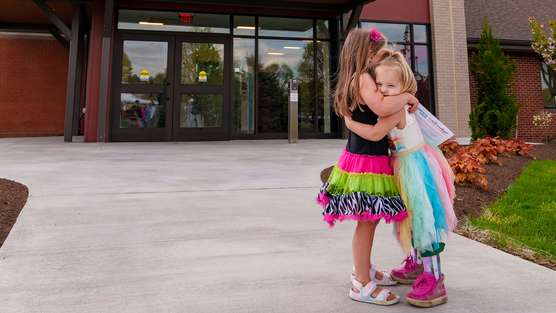 Two children in colorful dresses hugging in front of Schreiber Center.