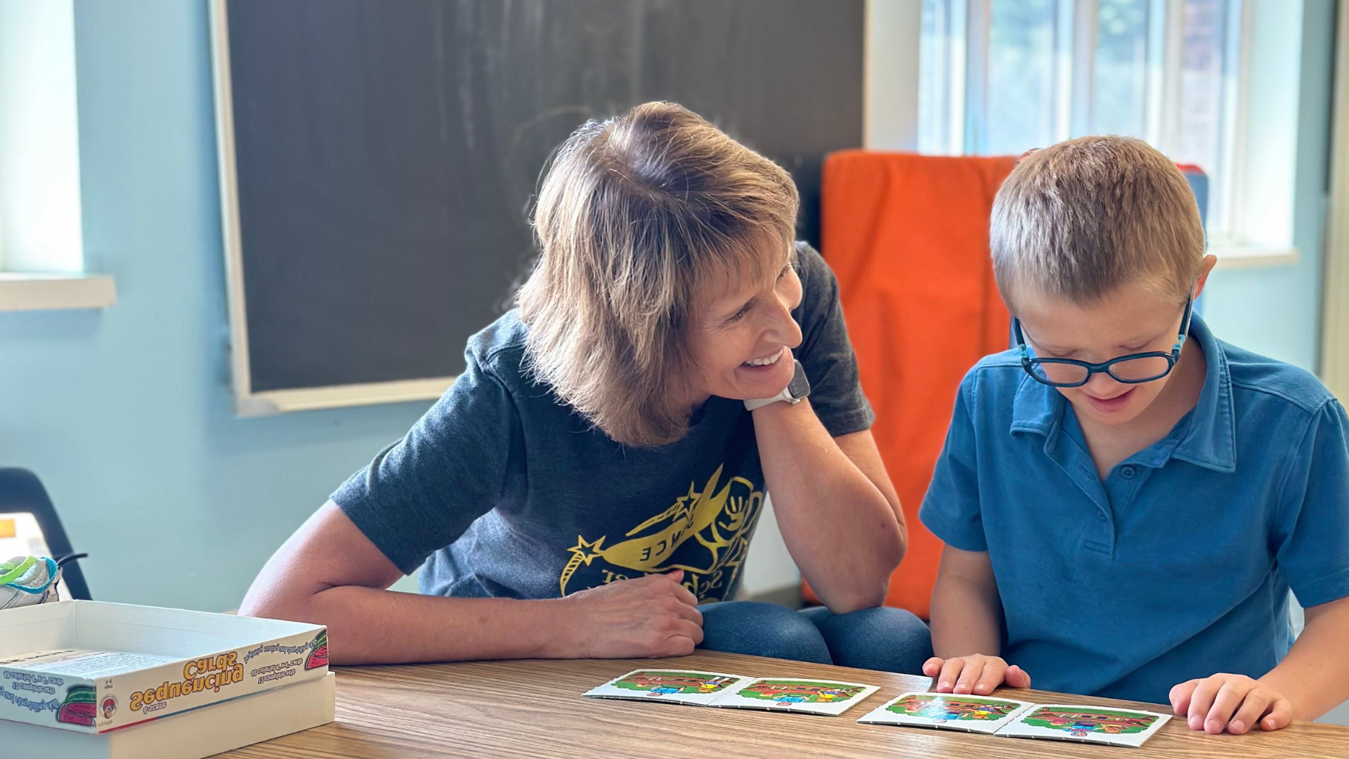 A therapist assisting a child working through a card excerise at a table.