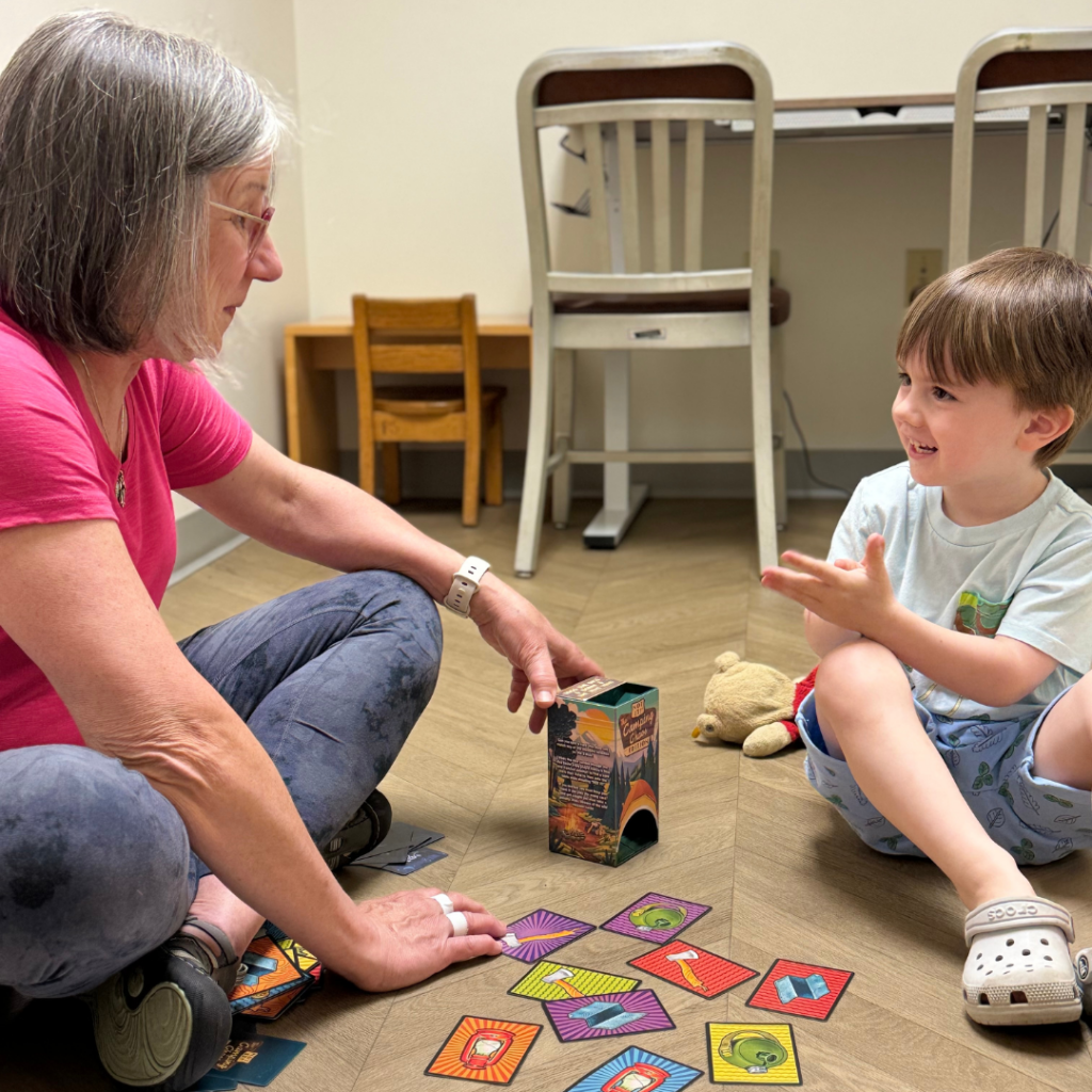 An occupational therapist and Grayson sitting on the floor with colorful cards depicting objects on the floor between them.