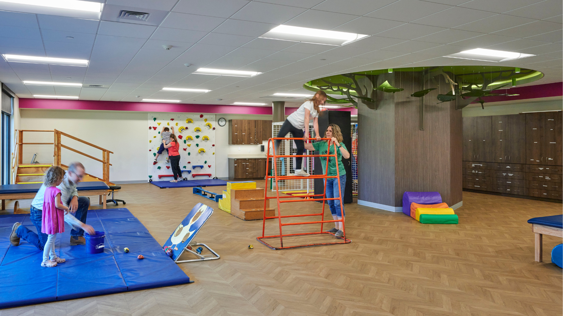 An expansive room with multiple areas for therapy exercises with children and therapists utilizing them.