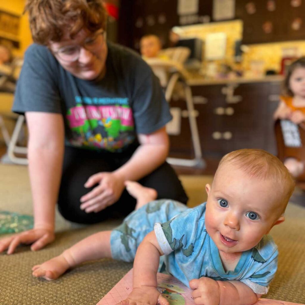 teacher playing with baby on the floor while looking into camera