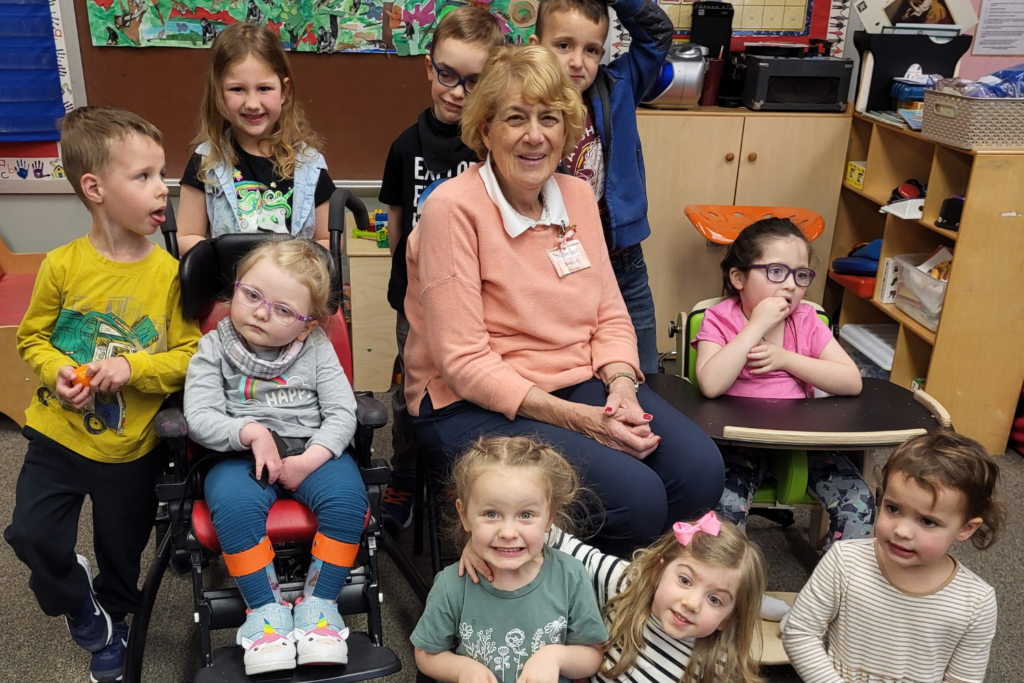 older woman sitting in chair surrounded by students