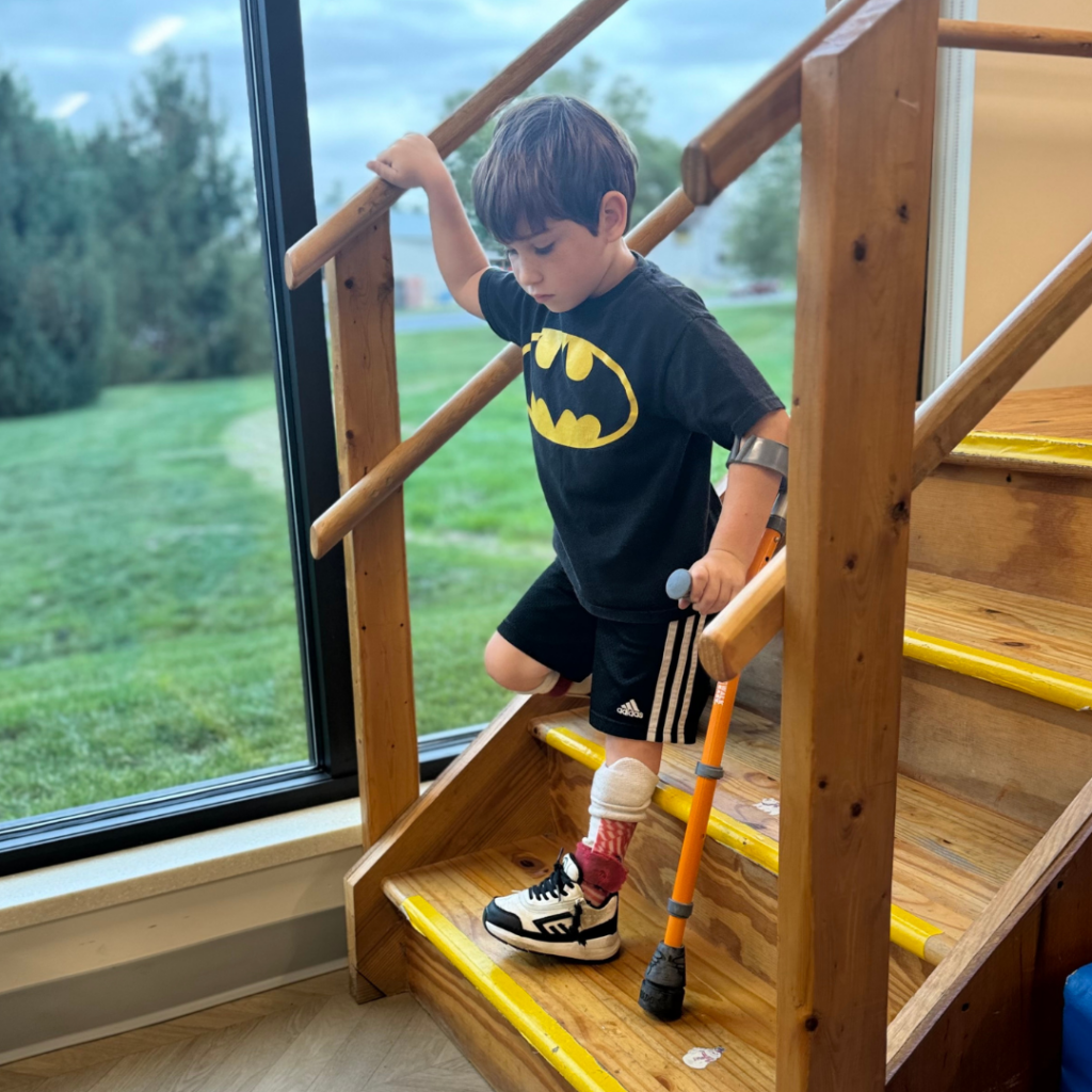 boy in a batman shirt walking down stairs with crutch