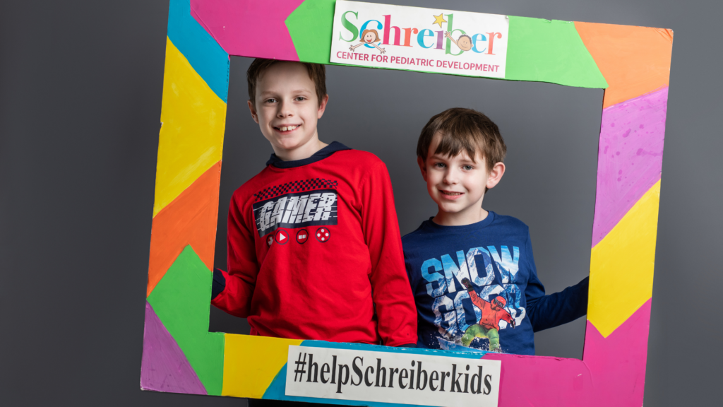 two boys posing for picture while holding up a colorful frame