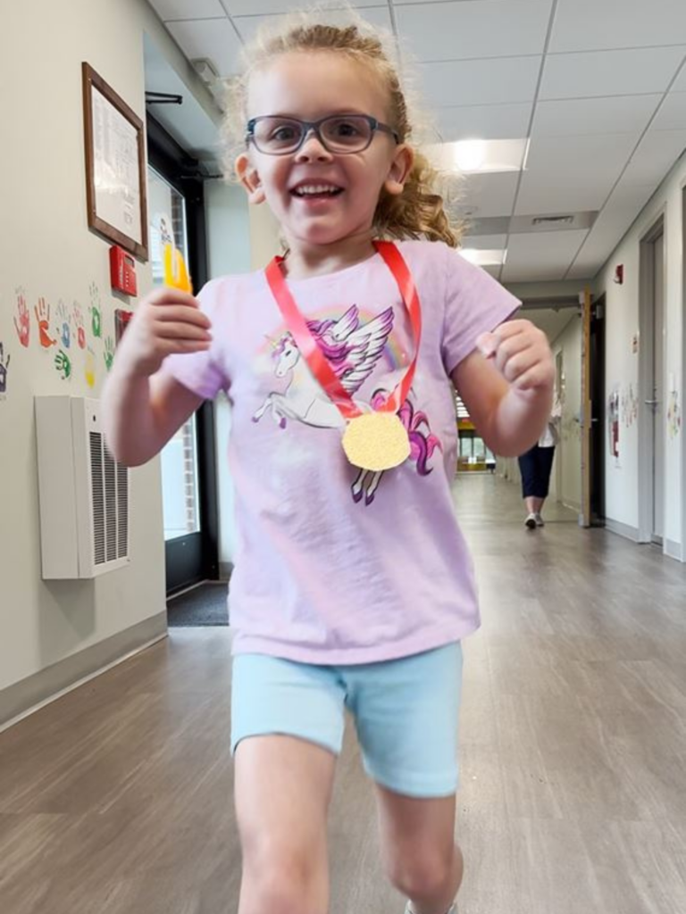 A child running toward the camera wearing a homemade medal around their neck.