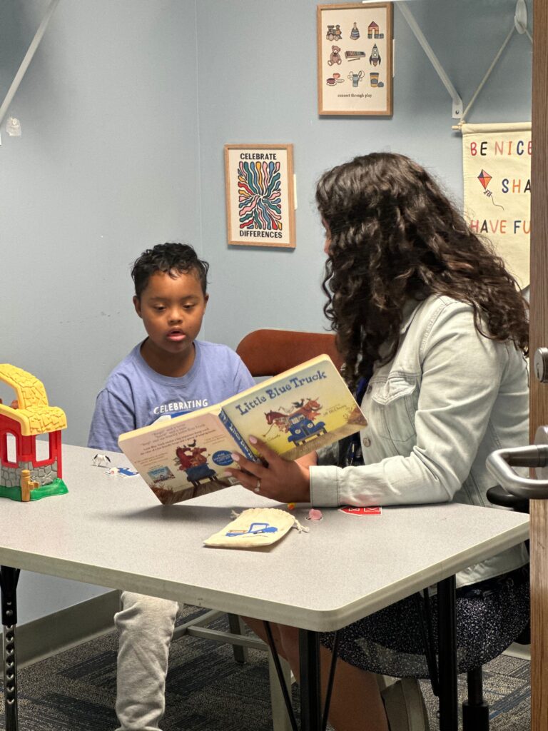 A therapist holds a book open while a child looks at the pages in a speech therapy exercise.