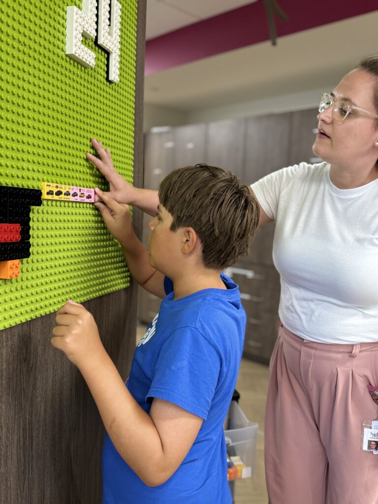 A kiddo working on an exercise using a pegboard on the wall with a therapist.