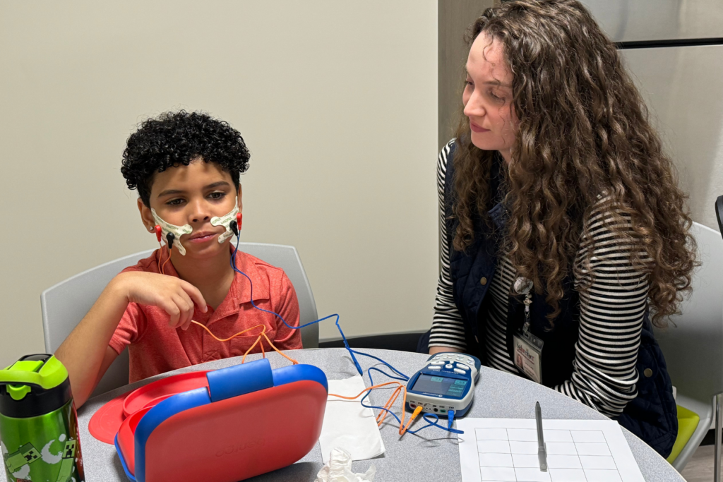 A child utilizing a vital stim therapy machine on their cheeks with a therapist assisting.