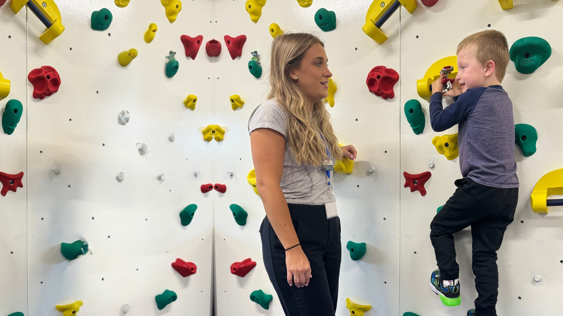 An adult supervising a child climbing a rock wall.