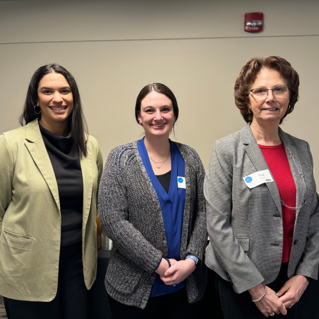 Three women with name tags in front of a brick wall smiling.